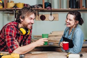 Man_and_girl_carpenters_having_break_from_indoor_work_in_wood_workshop._Coffee_time,_drink,_share_experiences,_discuss._Teacher_and_student._Laughing_smile.