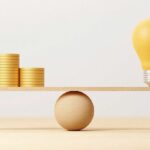 Coin_stack_compare_light_bulb_idea_on_wood_scale_seesaw._Money_gold_coin_compare_balance_with_knowledge_concept._3d_illustration