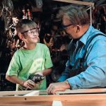 Young_boy_drilling_window_while_helping_grandfather_carpenter_in_workshop.
