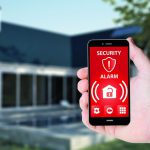 60013535_-_hand_hold_a_phone_with_security_alarm_app_on_a_screen_on_the_background_of_a_house.